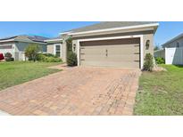 Front exterior of home with brick driveway and two-car garage with carriage door and well manicured landscaping at 841 Benjamin Trl, Davenport, FL 33837