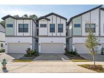 View of three-story townhomes, showing attached garages, manicured landscaping, and modern architectural design at 10364 Ebb Tide Ln, Orlando, FL 32821