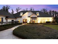 Elegant white home featuring manicured landscaping, arched entry and black roof at dusk at 1404 Kelso Blvd, Windermere, FL 34786