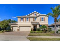 Two-story tan home with brick driveway, three-car garage, stone accents, manicured lawn, and lovely landscaping at 5142 Sage Cedar Pl, Sanford, FL 32771