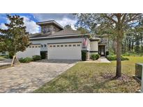 Charming home featuring a brick driveway, two-car garage, manicured lawn, and an American flag displayed on the front at 842 Aldenham Ln, Ormond Beach, FL 32174