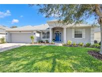 Charming single-story home featuring a well-manicured lawn, inviting blue door and a two car garage at 15320 Grand Haven Dr, Clermont, FL 34714