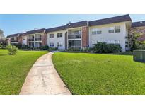 A view of the condo complex exterior with manicured lawn and concrete sidewalk leading to the building at 3800 Saxon Dr # 19B, New Smyrna Beach, FL 32169