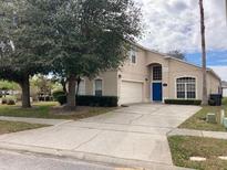 Two-story home with well-maintained front yard, featuring mature trees and a paved driveway leading to a two-car garage at 954 Lockbreeze Dr, Davenport, FL 33897