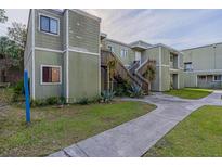 A weathered two-story exterior with a concrete walkway, lawn, and wood stairs that lead to the front door at 101 Scottsdale Sq # 101, Winter Park, FL 32792