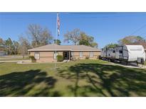 Single-story tan home with a well manicured lawn, American flag, and camper parked in the driveway at 5347 Pecan Rd, Ocala, FL 34472