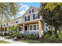 Charming two-story home featuring tan stucco, black shutters, and a welcoming front porch with white railings and manicured landscaping at 9228 Cardinal Meadow Trl, Orlando, FL 32827