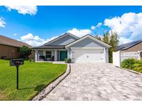 Charming single-story home features a well-manicured lawn, paver driveway, and a welcoming covered porch with seating at 127 Thorne Meadow Pass, Davenport, FL 33897