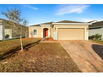 Charming single-story home featuring a brick driveway, neutral tones, and a red front door at 2015 Sloans Outlook Dr, Groveland, FL 34736