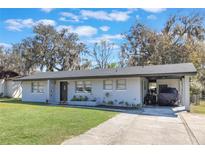 Charming single-story home featuring a brick facade, well-maintained lawn, and covered parking area with mature trees at 2303 Mahoney Ave, Leesburg, FL 34748