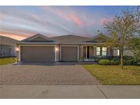 Charming single-story home with a well-maintained lawn, mature landscaping, and a brick paver driveway leading to a two-car garage at 103 White Horse Way, Groveland, FL 34736