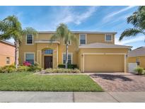 Two-story home boasting a manicured lawn, mature palm trees, and a brick driveway at 174 Yellow Snapdragon Dr, Davenport, FL 33837