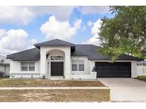 Inviting single-story home with a dark roof, black door, a two-car garage, and manicured landscaping at 2930 Paddington Way, Kissimmee, FL 34747