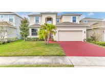 Charming two-story home featuring a manicured lawn, vibrant landscaping, and a red brick driveway leading to an attached garage at 2246 Rush Bay Way, Orlando, FL 32824