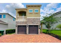 Charming two-story home featuring a stone facade, balcony, and a two-car garage with brick paver driveway at 7717 Graben St, Kissimmee, FL 34747