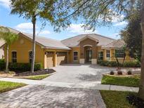 Stunning yellow home featuring a tile roof, three-car garage, brick paver drive, and manicured landscaping at 3850 Eagle Isle Cir, Kissimmee, FL 34746