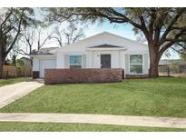 This house features a white exterior, complemented by lush lawn, sidewalk, and a brick accent wall at 6222 Fox Hunt Trl, Orlando, FL 32808