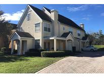 A cream-colored townhome with a brick driveway, green lawn, and manicured bushes set against a blue sky at 6593 Queens Borough Ave # 201, Orlando, FL 32835