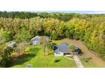 Aerial view of a charming single-story home with a gray roof, set on a lush green lawn surrounded by mature trees at 20639 Sw Rainbow Lakes Blvd, Dunnellon, FL 34431