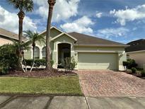 Charming home showcasing tropical landscaping, a brick driveway, and an attached two-car garage at 1923 Willow Wood Dr, Kissimmee, FL 34746