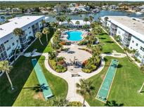 Aerial view showcasing a community with a pool, shuffleboard courts, and fire pit amidst lush landscaping and waterfront access at 325 N Causeway # 2080, New Smyrna Beach, FL 32169