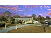 Inviting single-story home with a well-manicured lawn, mature trees, and a long driveway leading to the attached garage at 5170 Ne 64Th Ave, Silver Springs, FL 34488