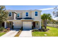 Two-story tan townhome featuring an attached garage, lush lawn, and a vibrant palm tree at 10849 Wyne Tree Ct, Orlando, FL 32824