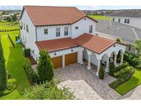 An exterior view of a two-story white house, featuring a terracotta tile roof, manicured landscaping, and a brick driveway at 8025 Topsail Pl, Winter Garden, FL 34787