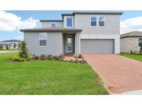 Charming two-story home with a well-manicured lawn and a brick driveway leading to the garage at 2933 Wild Olive Dr, St Cloud, FL 34772