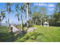 Lush backyard featuring a dock on the water, verdant lawn, trees, and a charming white gazebo at 703 Valencia Shores Dr, Winter Garden, FL 34787
