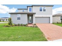 Two-story home with gray siding, brick driveway, manicured lawn, and integrated two-car garage at 2917 Wild Olive Dr, St Cloud, FL 34772