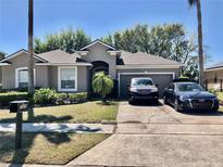 Well-maintained gray house with tidy landscaping, two-car garage, and paved driveway with two parked vehicles at 1838 Palmerston Cir, Ocoee, FL 34761