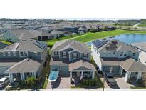 Aerial view of a two-story home with a manicured lawn in a lakeside community with solar panels on several houses at 10732 Petrillo Way, Winter Garden, FL 34787
