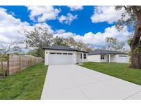 Modern home featuring a long driveway, two-car garage, and minimalist landscaping with green grass and vibrant trees at 1104 Grove Manor Dr, Sanford, FL 32771