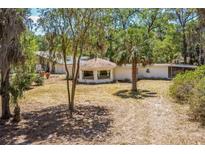 Exterior view of a white home featuring a distinctive round sunroom and a natural landscape with mature trees at 450 Cassady St, Umatilla, FL 32784
