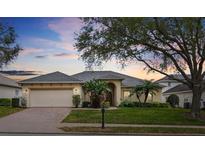 Charming one-story home with a well-manicured lawn, mature trees, and a brick-paved driveway leading to a two-car garage at 548 Burford Cir, Davenport, FL 33896