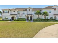 Well-manicured townhouse with lush green lawn, featuring a covered entryway and mature palm trees at 8959 Stinger Dr, Champions Gate, FL 33896