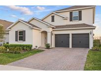 Two-story home with a two-car garage, brick driveway, manicured landscaping, and neutral exterior at 4778 Cragmere Loop, Clermont, FL 34711