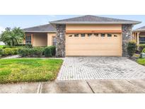 Charming single-story home featuring a beige exterior, stone accents, and a brick paver driveway and walkway at 253 Lake Cassidy Dr, Kissimmee, FL 34759