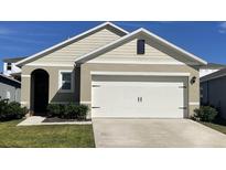 Beige one-story home with a two-car garage and well-kept lawn, perfect for suburban living at 3651 Salvia Ct, Tavares, FL 32778