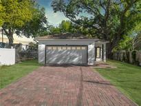 View of the home's attached garage and the brick paver driveway, surrounded by manicured lawn and mature trees at 1505 25Th St, Orlando, FL 32805