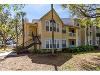 Inviting yellow condo with black staircase, mature trees, and well-maintained landscaping for a serene outdoor experience at 1017 S Hiawassee Rd # 3718, Orlando, FL 32835