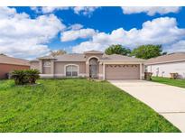 Charming single-story home with a two-car garage, arched entryway, and landscaped front yard under a blue sky at 142 Barrington Dr, Kissimmee, FL 34758