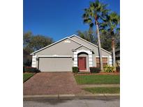 Charming home features a red front door, brick driveway, gray siding, and well-maintained landscaping with palm trees at 1457 Waukon Cir, Casselberry, FL 32707