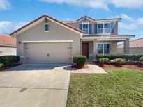 Two-story home with red tile roof, tan exterior, blue shutters, landscaping, and a two car garage at 3056 Sangria St, Kissimmee, FL 34744