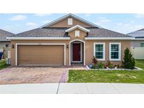 Tan single-story home with a red-brick driveway, tidy landscaping, and an attached two-car garage at 434 Ironside Trail Dr, Groveland, FL 34736
