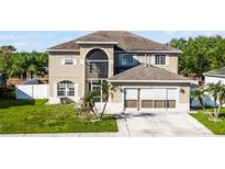 Beige two story home with a front yard, two-car garage, and arched windows at 5456 Crepe Myrtle Cir, Kissimmee, FL 34758