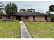 Charming brick home with a well-manicured lawn, walkway, and mature palm trees at 635 Malaga Ave, Deltona, FL 32725