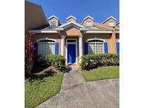 Charming townhome featuring a bright blue front door, white pillars, dormer windows, and lush landscaping at 1920 Island Walk Dr, Orlando, FL 32824