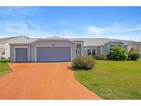 Charming single-story home featuring a three-car garage, mature landscaping, and a colorful driveway at 5414 Zinnia St, Leesburg, FL 34748